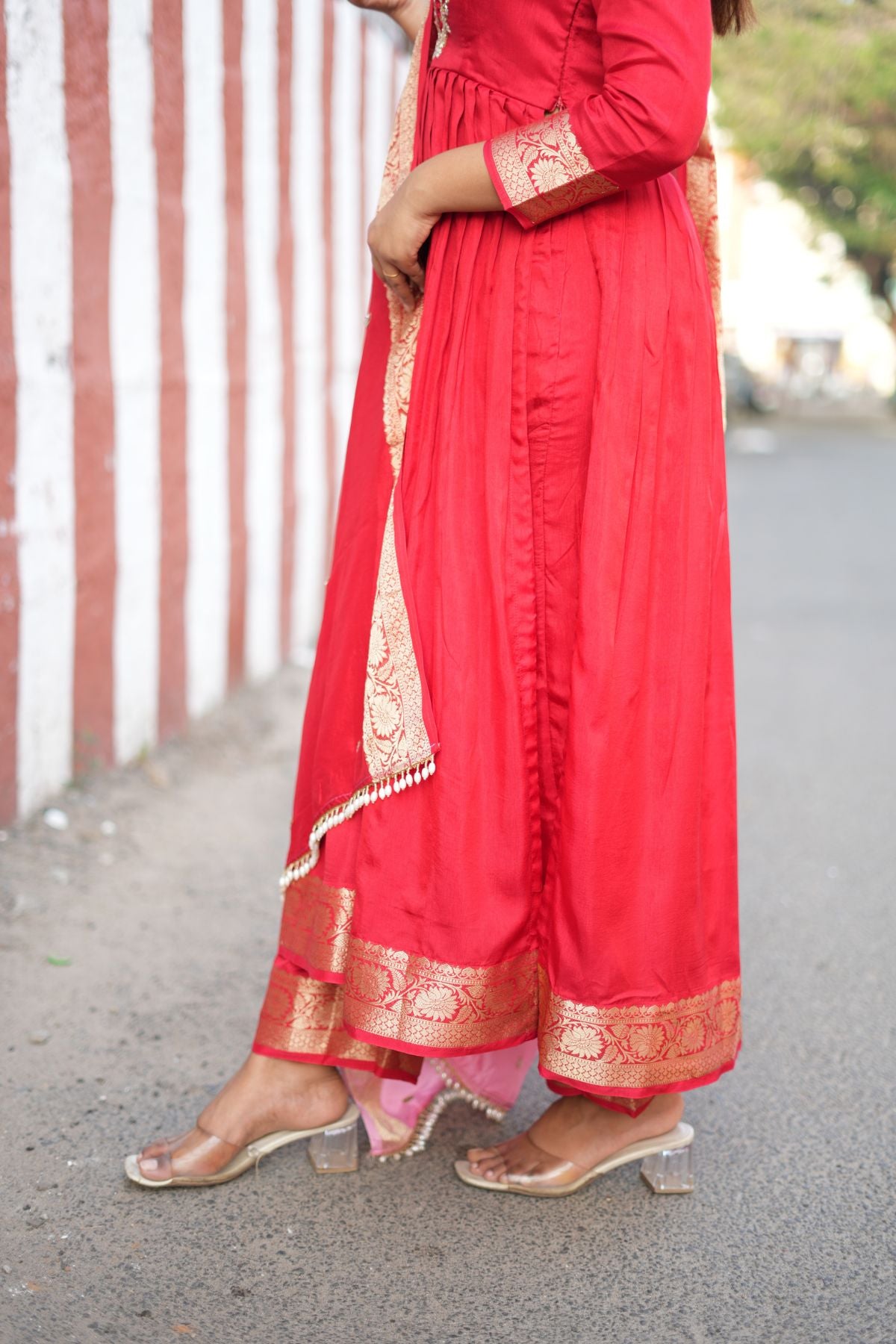 Close-up of the hemline and footwear with Madhubala Silk Kurta Set in Red, highlighting the golden Banarasi border. A stylish ethnic dress for formal wear.