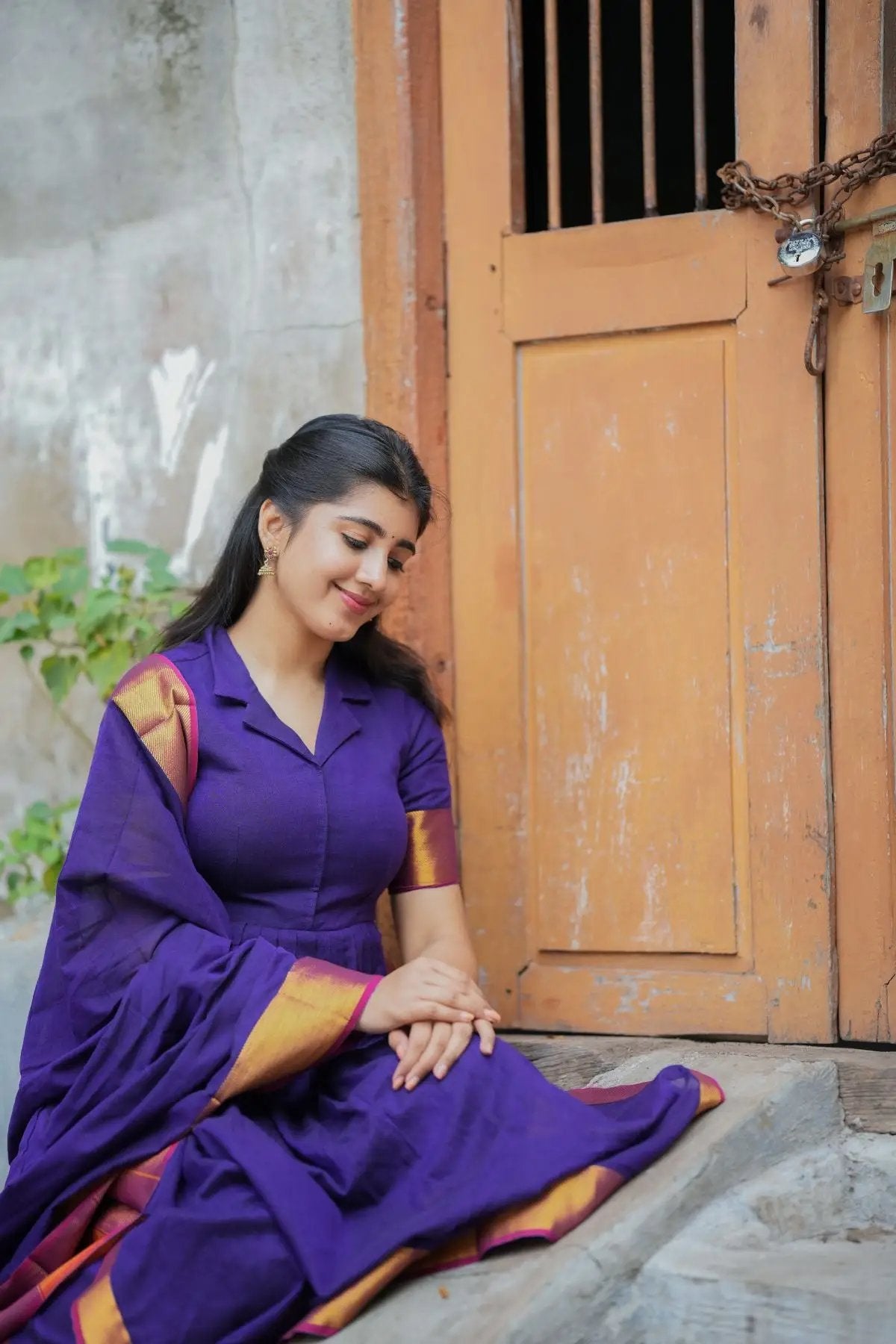 Seated model in purple handloom suit set by wooden door