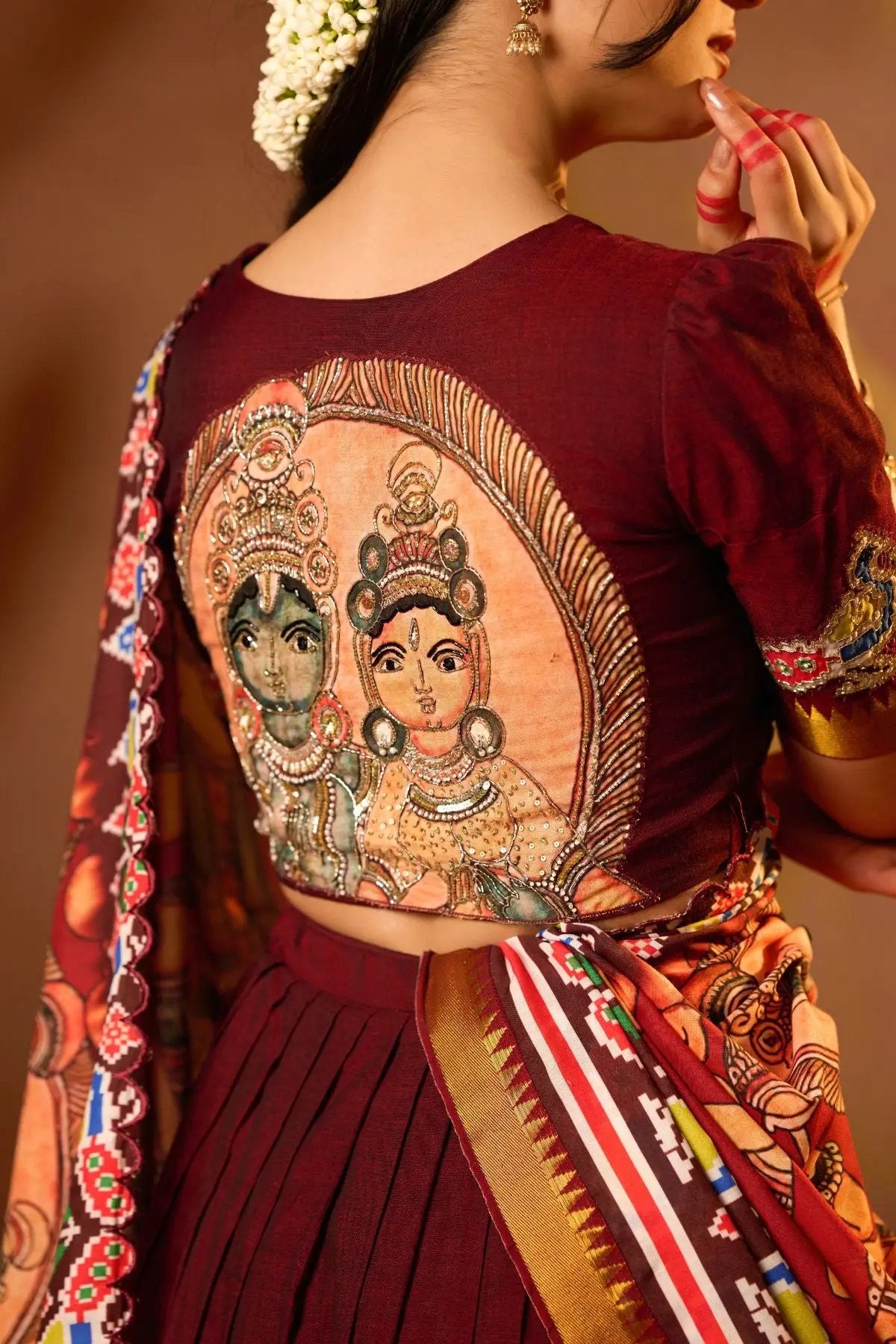 Back view of the Sitaramam Lehenga Set in Maroon showcasing a detailed embroidered blouse with divine artwork, paired with a richly designed dupatta.