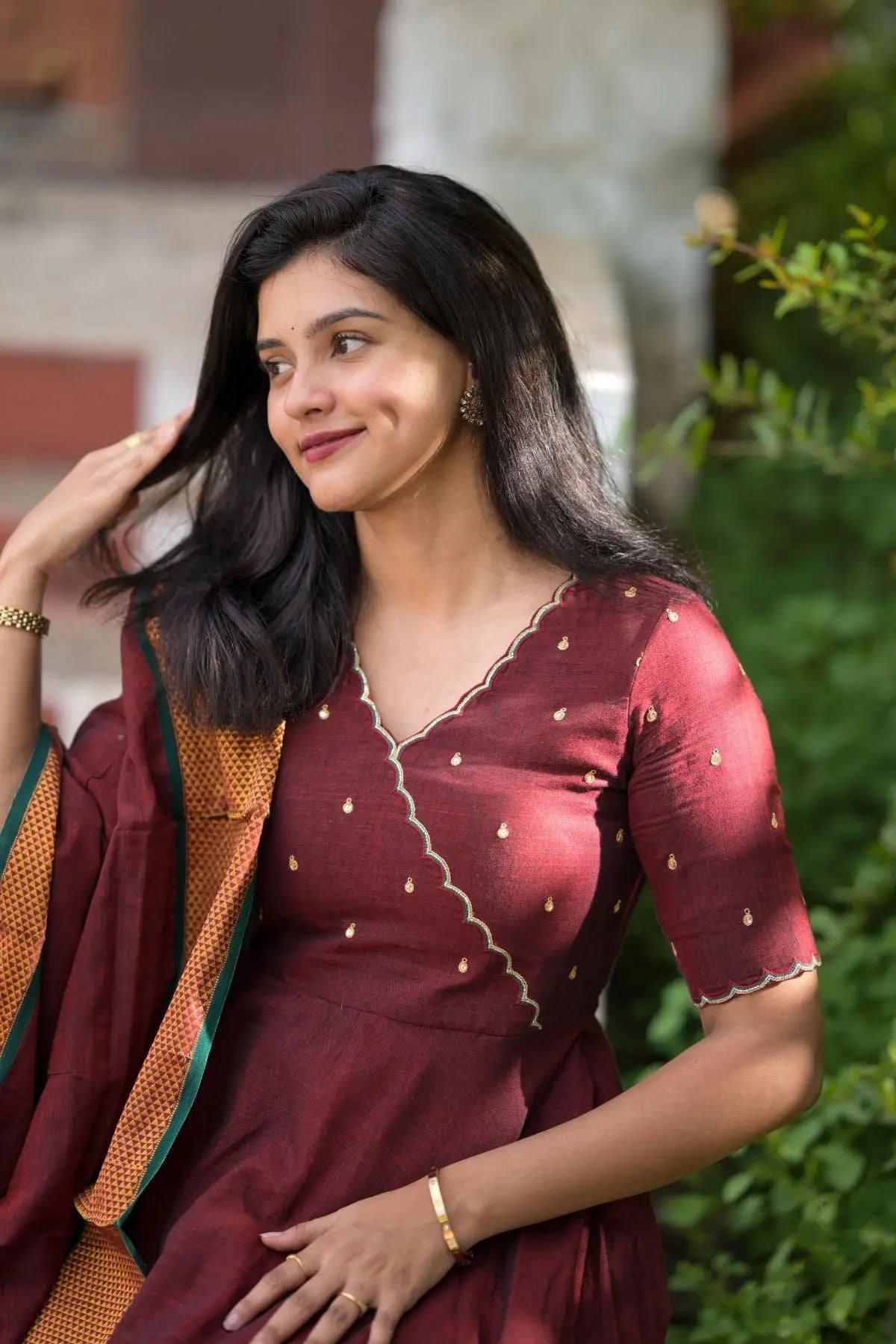 Maroon dress with golden details, woman adjusting hair