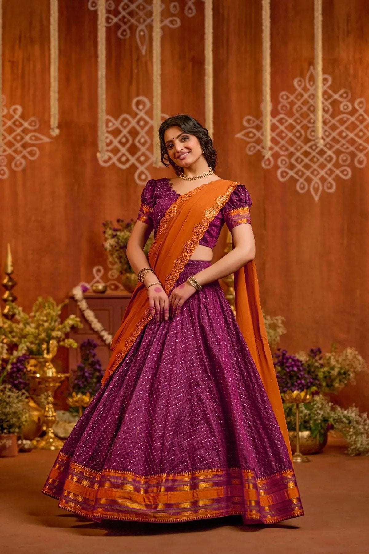 Exclusive Vairagi Naraynpet Lehenga Set in purple with intricate gold detailing and an orange dupatta, perfect for traditional occasions.