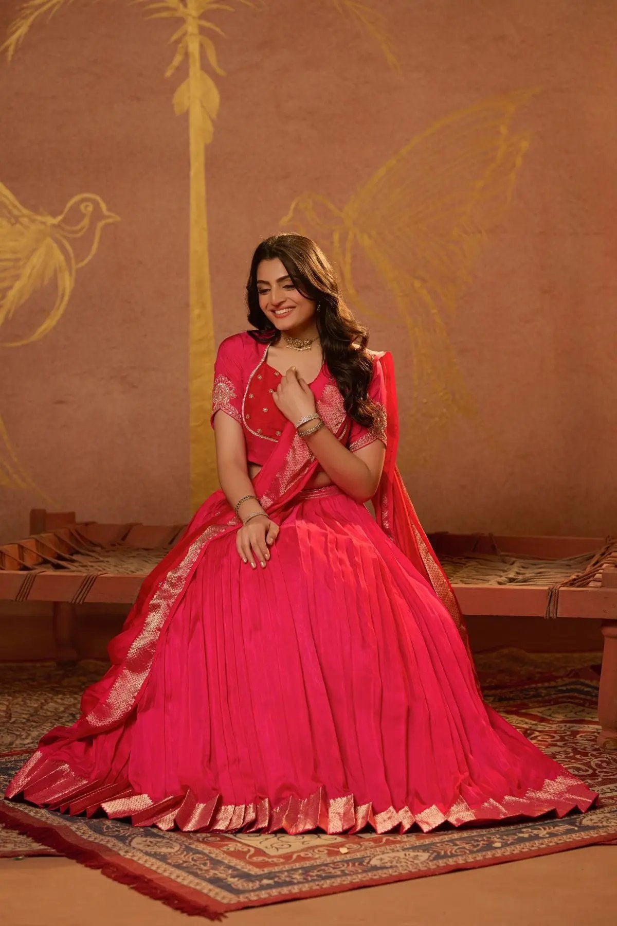 Seated pose of a model in the Pritti Lehenga Set in Rani Pink, highlighting the grandeur of the pleated skirt and traditional embroidery.