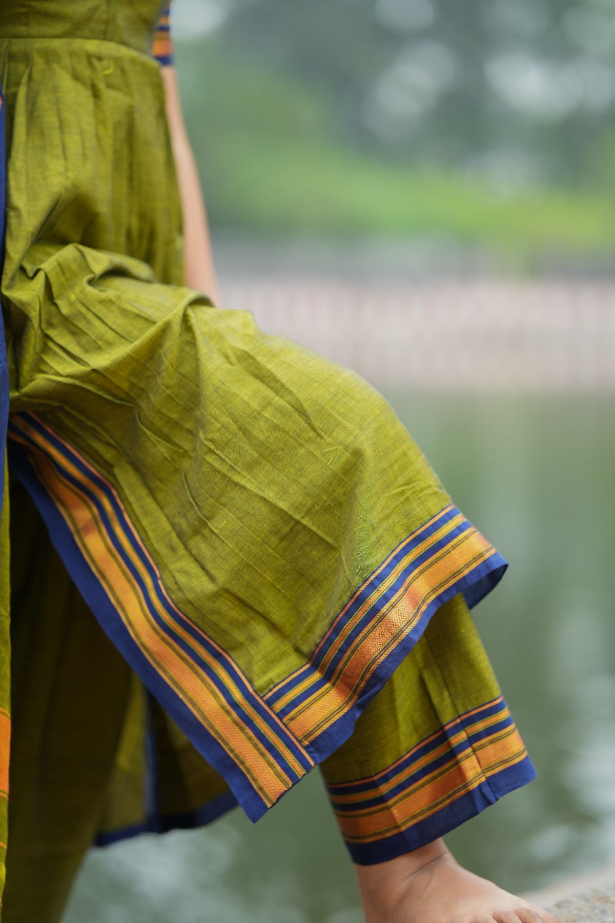 Close-up of Syahi Handloom Suit Set in olive green, showcasing the detailed striped border on the pants. Traditional elegance available at bullionknot.