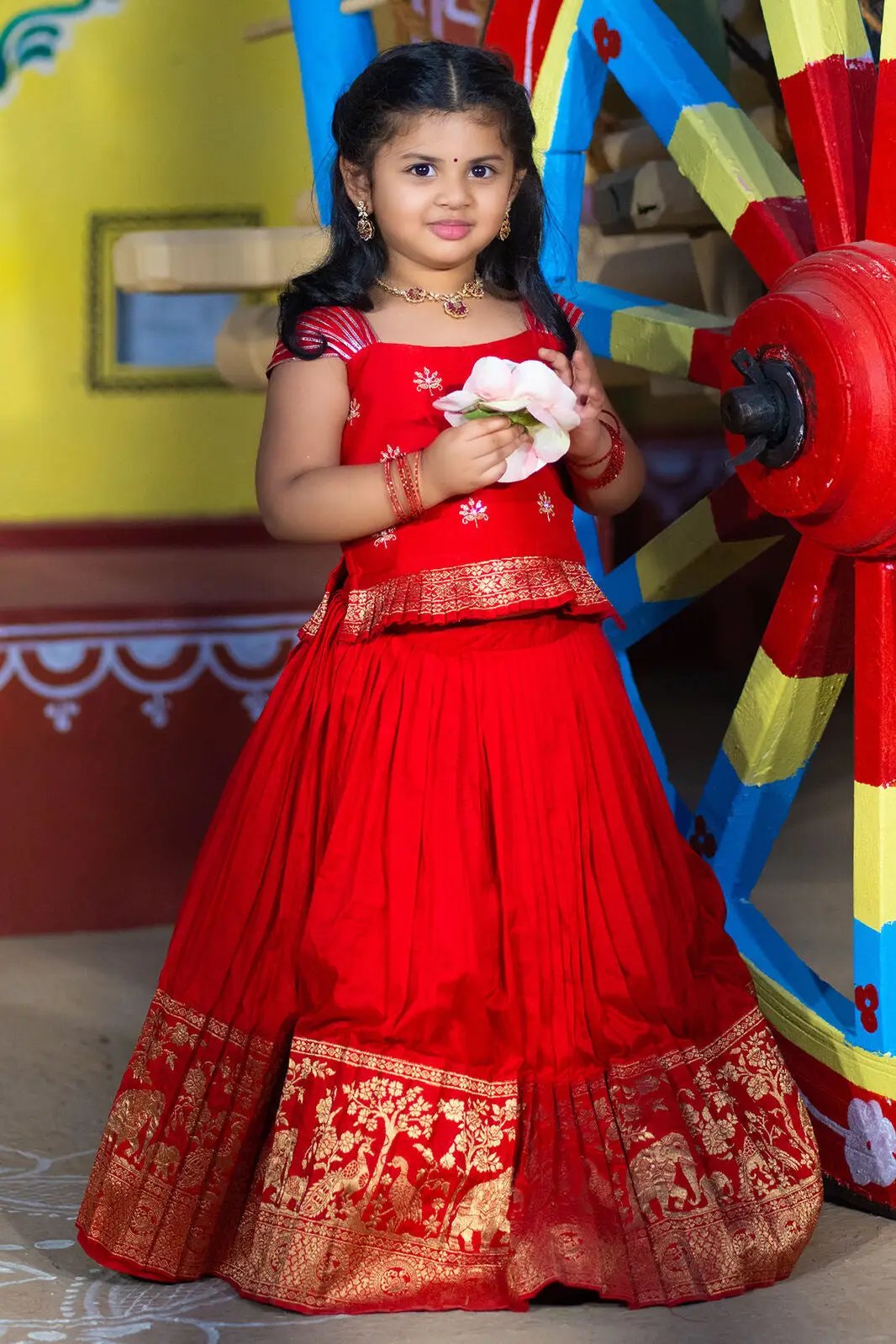 Child wearing red Baby Rani Lehenga Set holding flowers