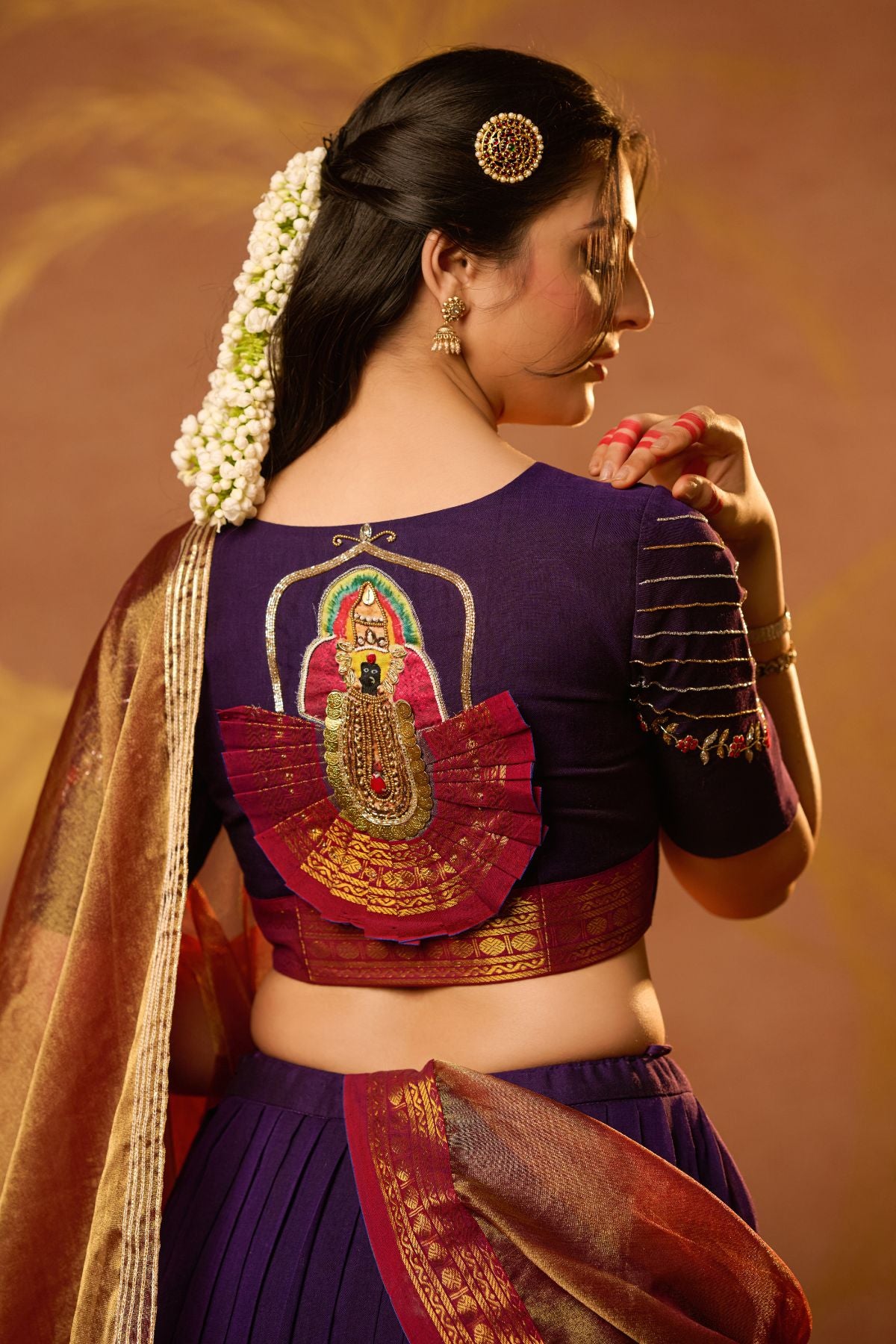 Back view of Mahalaxmi Lehenga Set in Purple showcasing embroidered deity motif on blouse. Paired with a golden zari dupatta for a regal look.