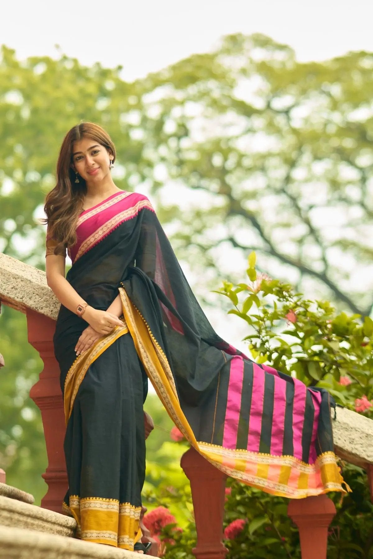 Gomti Handloom Saree in black with pink and gold border, styled elegantly on a model outdoors near a staircase.