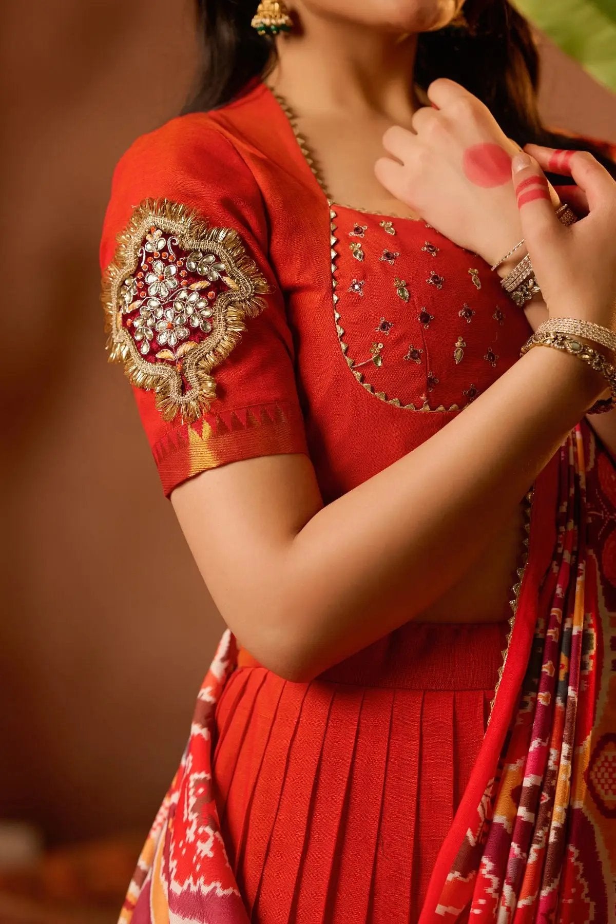 Close-up of Nakshatra Lehenga Set in orange, showcasing detailed embroidery on the blouse sleeve and elegant pleated skirt for a regal look.