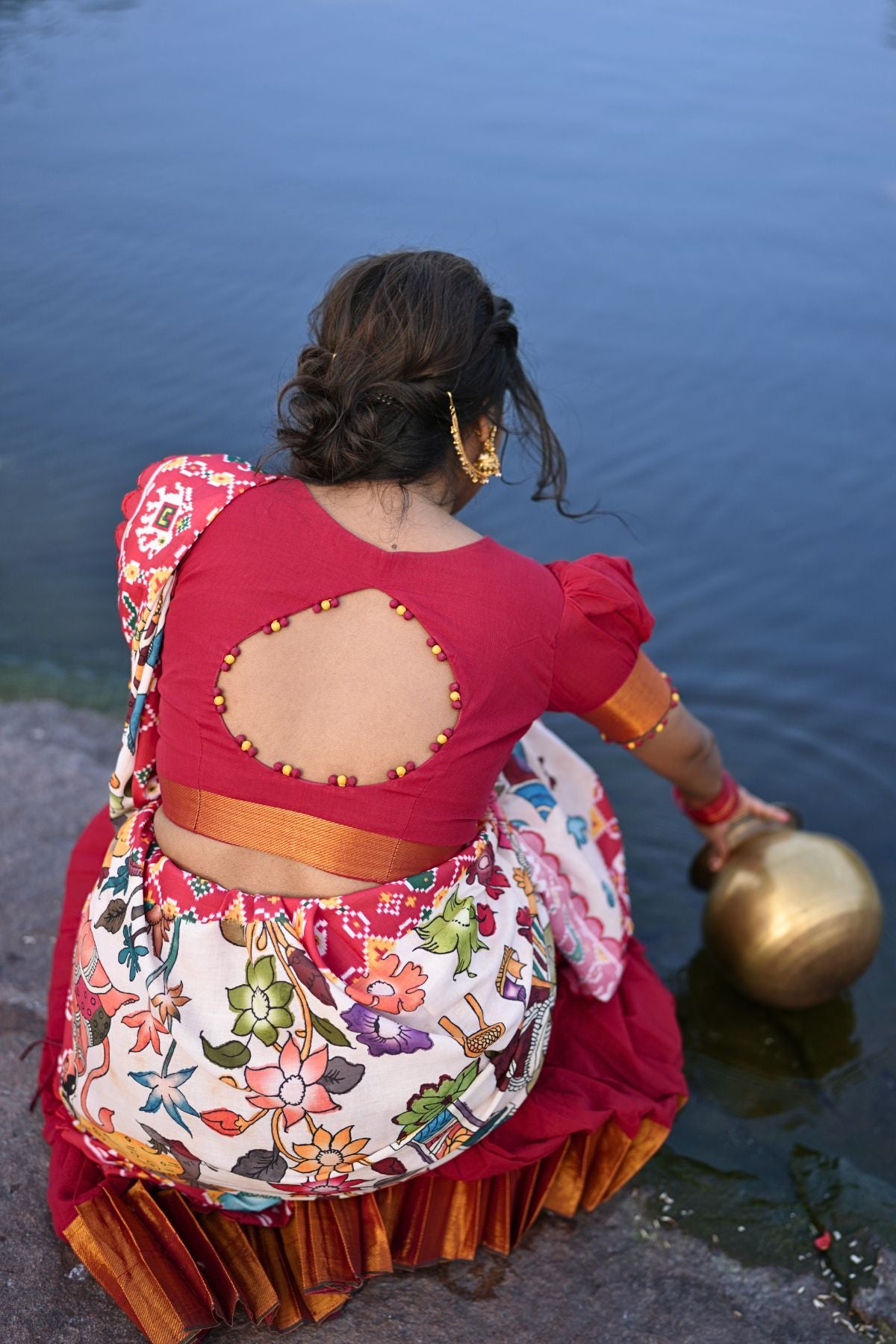 Back view of the Revti Handloom Lehenga Set in Red highlighting the cut-out blouse design and floral dupatta near a water body.