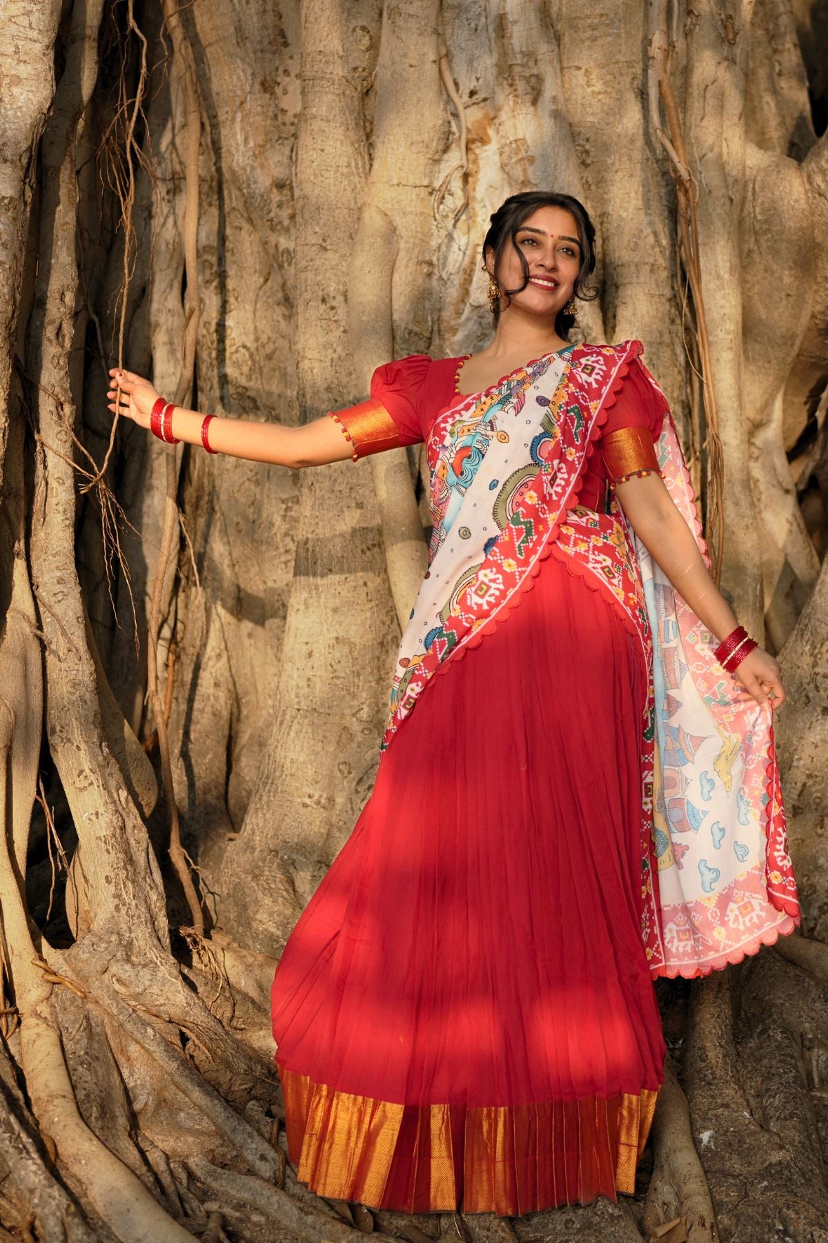 Traditional Revti Handloom Lehenga Set in Red with golden border and multicolor dupatta, styled elegantly against a tree backdrop.