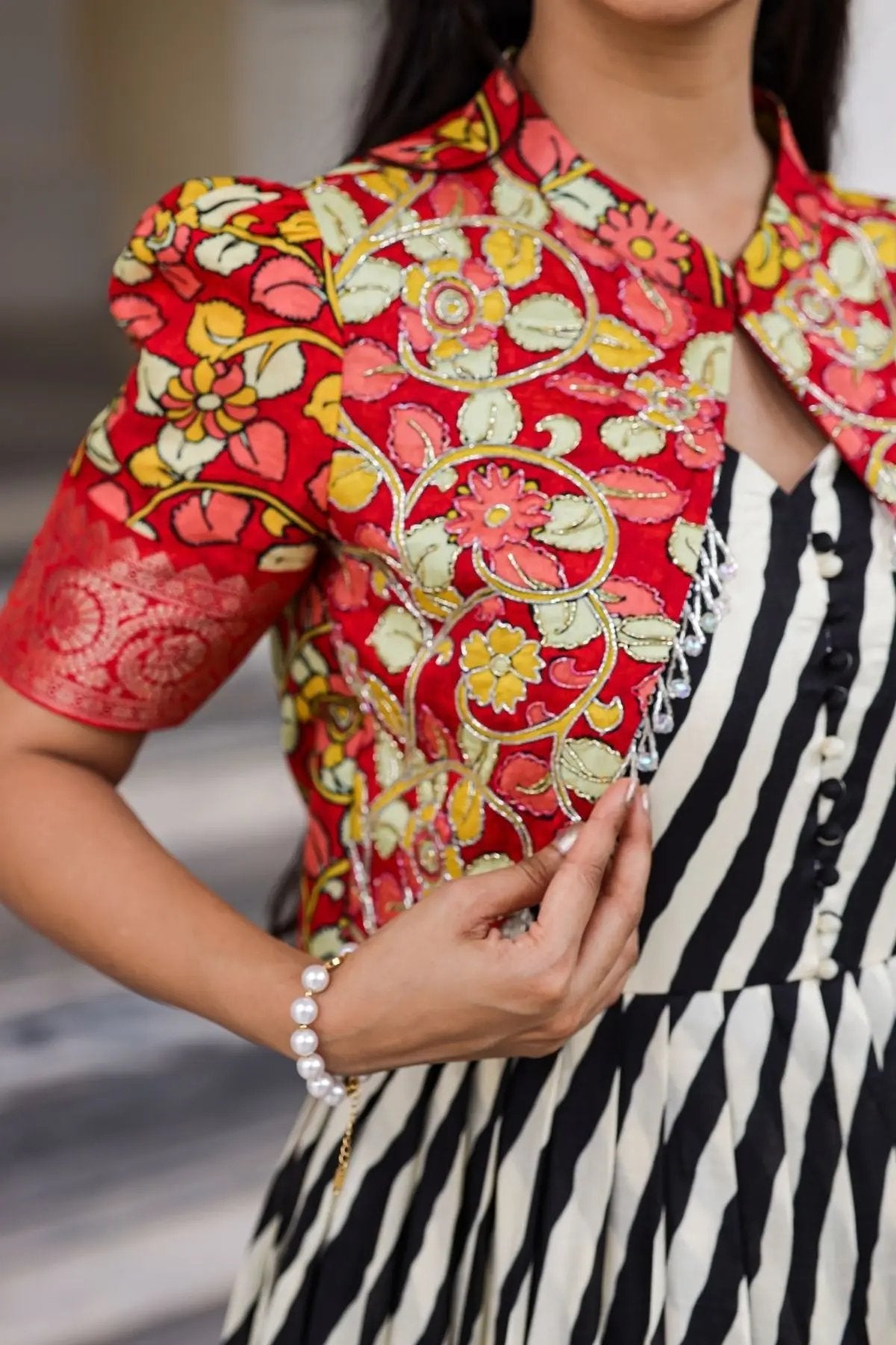 Close-up of the Rohini Kalamkari Jacket Dress showcasing intricate floral embroidery on the red jacket paired with a striped black-and-white dress.