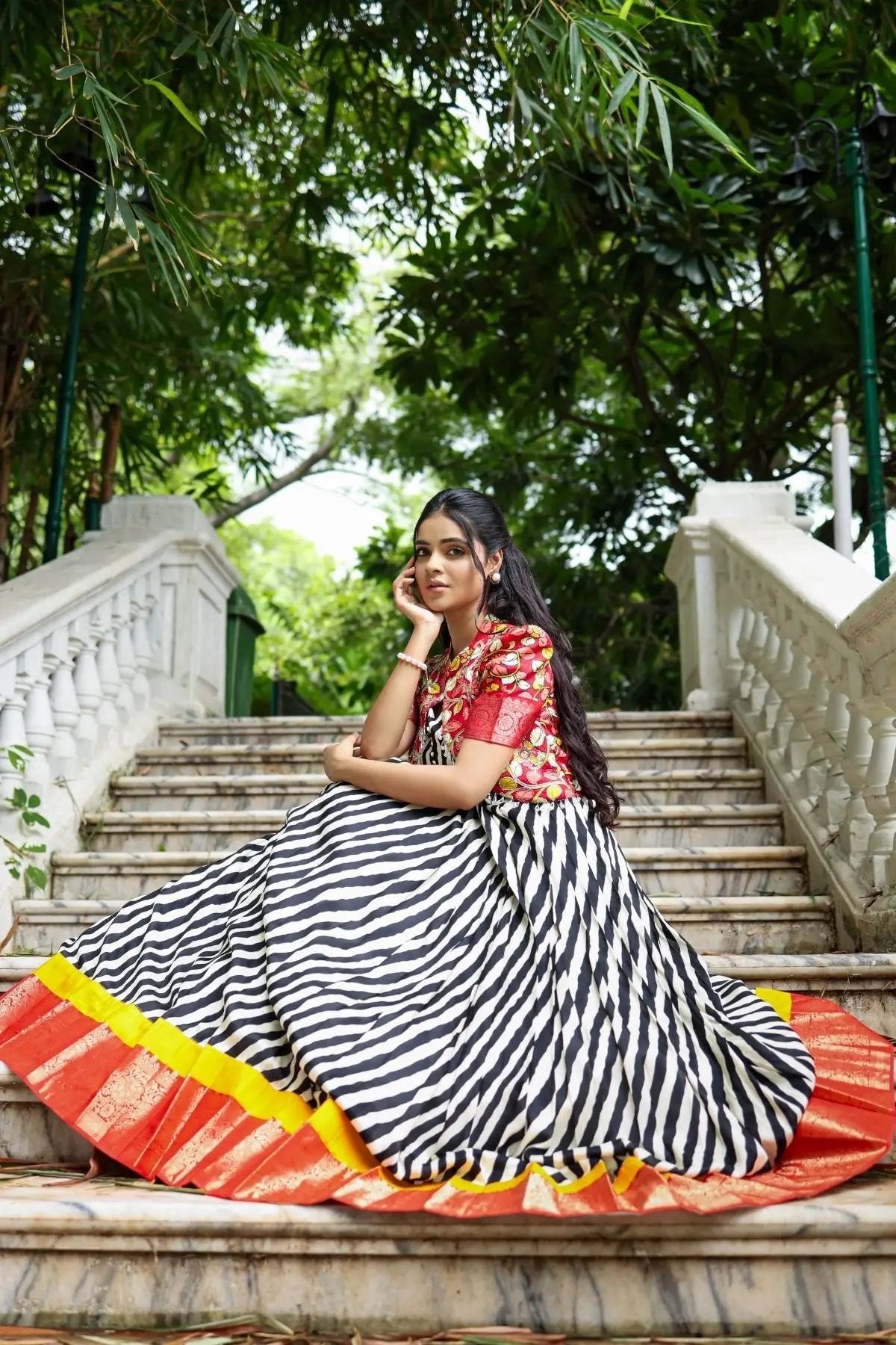 Elegant Rohini Kalamkari Jacket Dress in black with a bold striped skirt and colorful accents, styled on a staircase amidst lush greenery.