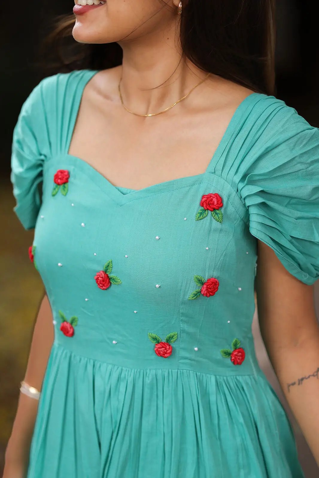 Close-up of aqua dress with red floral embroidery and puff sleeves.