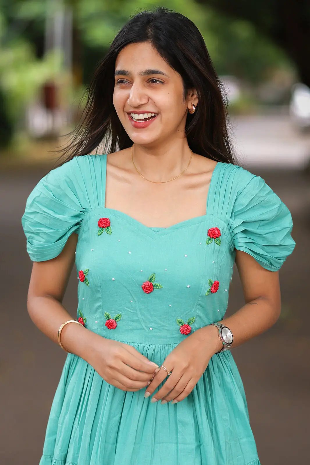 Smiling woman in aqua dress with red floral details and puff sleeves.