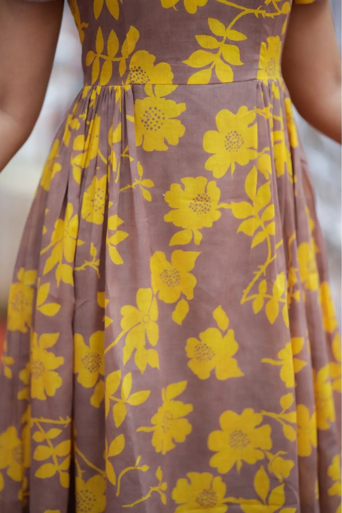 Close-up of Yelena Midi Dress skirt section, featuring vibrant yellow floral prints and pleated accents.