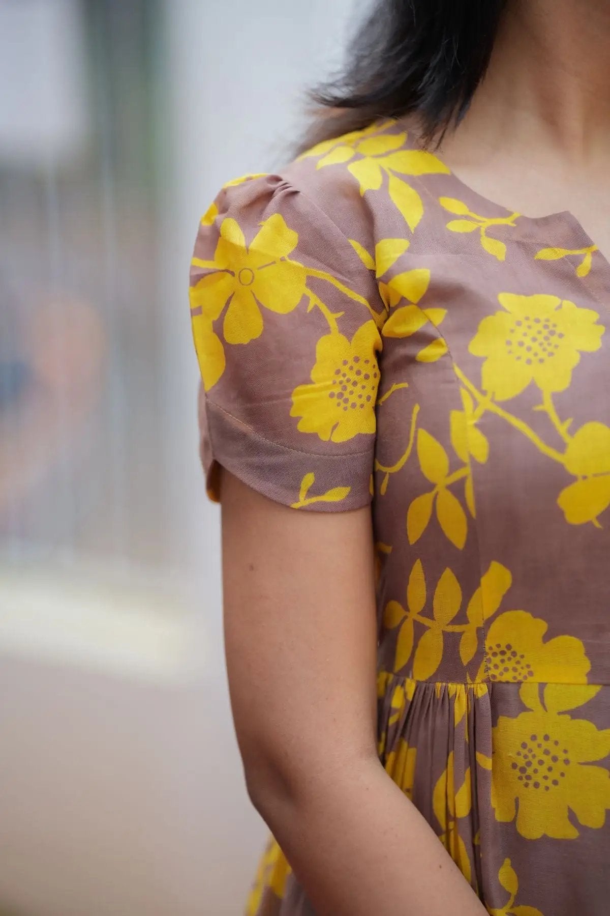 Close-up of Yelena Midi Dress showcasing yellow floral patterns on a brown base with puff sleeves and pleated details.